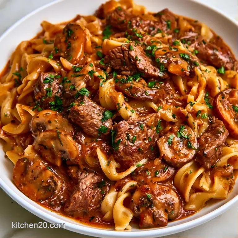 Creamy mushroom and beef strips nestled on swirling noodles in a white ceramic bowl with a sprinkle of fresh parsley.