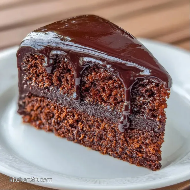 A thick slice of dark chocolate cake on a white porcelain plate, garnished with a fresh raspberry and mint leaf.